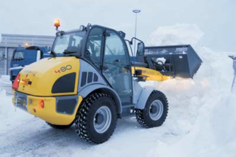 Gul traktor med snöskopa arbetar vid snöhög