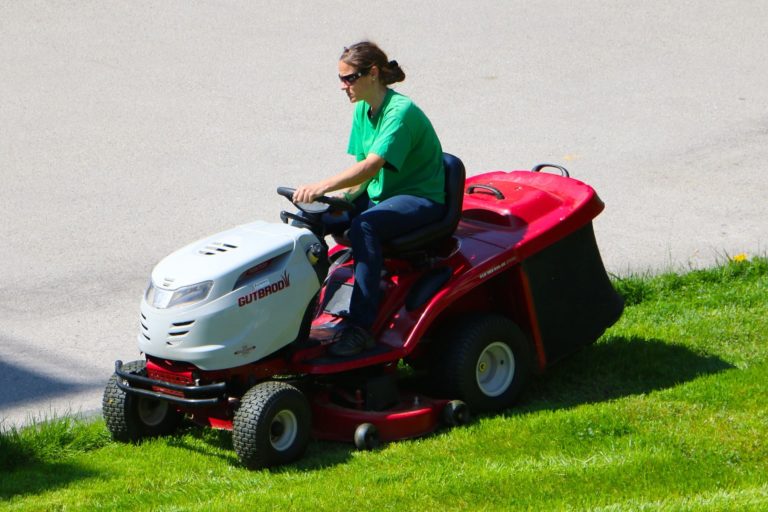 En parkarbetare kör professionell röd gräsklippare med ratt på en gräsmatta