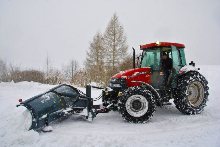 Röd traktor med snöplog röjer snö utomhus